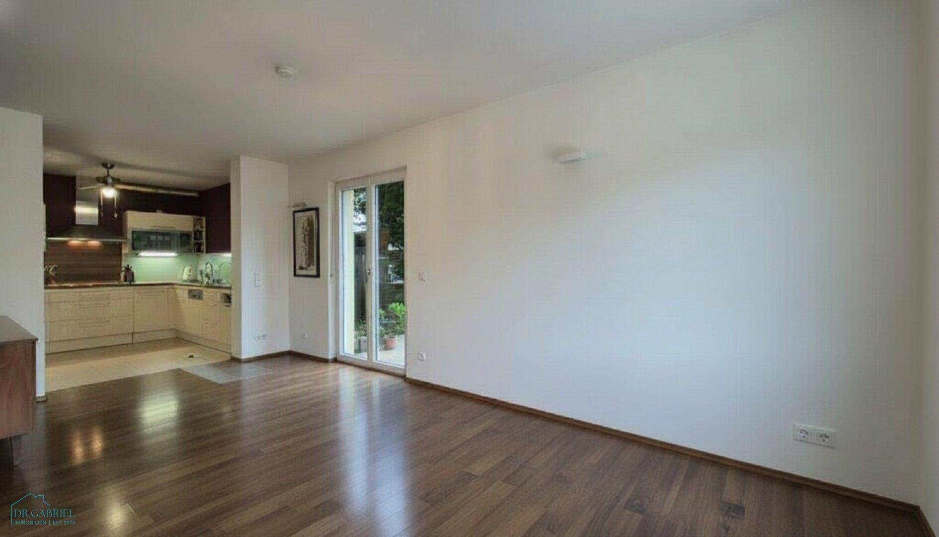 Offener Wohnbereich mit Holzboden und Blick auf die angrenzende Küche, mit Zugang zur Terrasse.