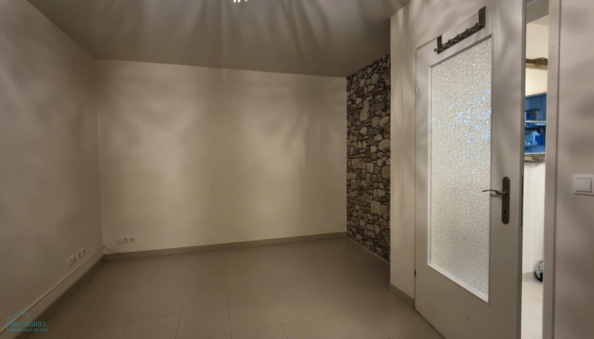 Leerer Raum mit Fliesenboden und einer Akzentwand aus Naturstein, bereit zur individuellen Gestaltung.