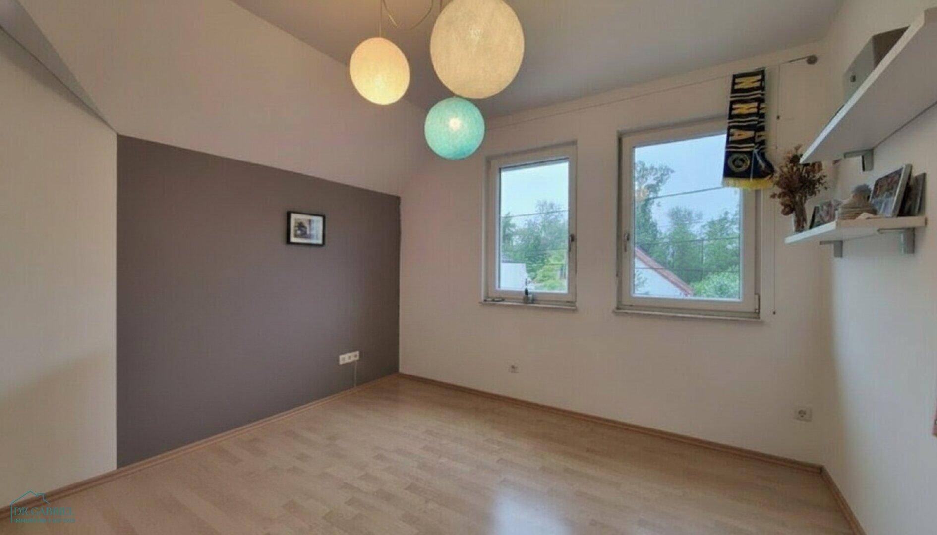 Helles Dachgeschosszimmer mit Holzboden und zwei Fenstern, ideal als Kinder- oder Gästezimmer.
