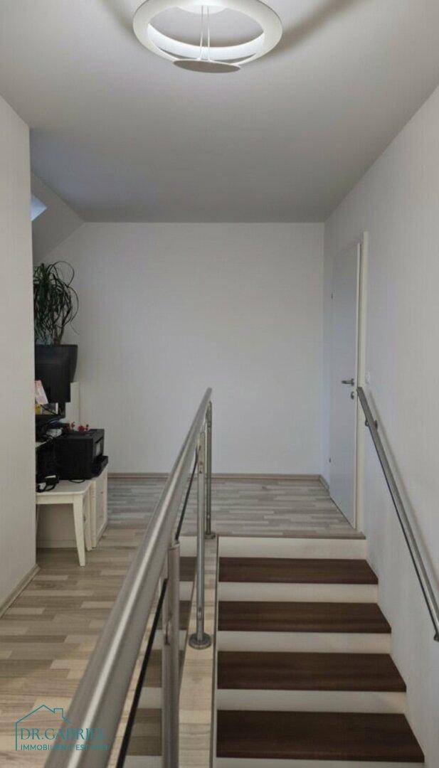 Heller Treppenaufgang mit modernem Geländer und Holzboden, führt ins Obergeschoss.