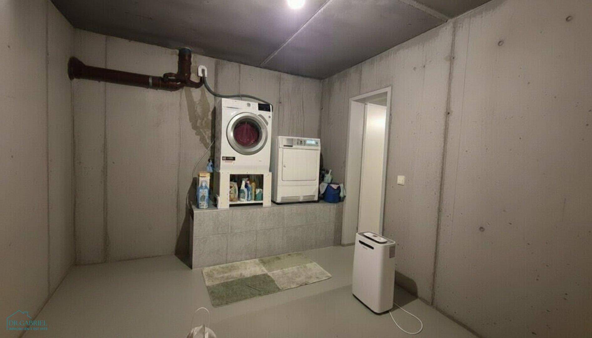 Funktioneller Hauswirtschaftsraum im Keller mit Waschmaschine und Trockner auf einem Podest.