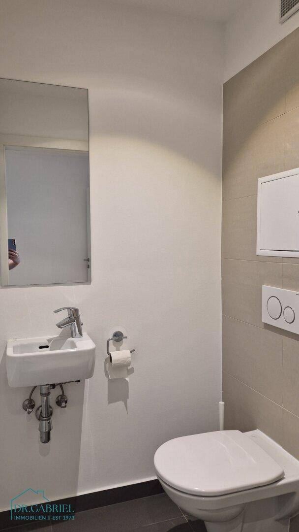 Funktionale Gästetoilette mit wandhängendem WC und kleinem Waschbecken, schlicht und sauber.
