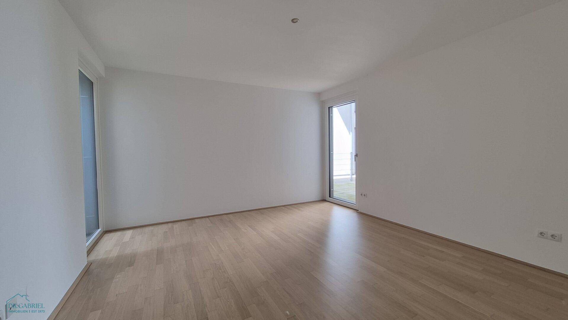 Helles, leeres Schlafzimmer mit Parkettboden und großen Fenstern, bietet viel Gestaltungspotenzial.