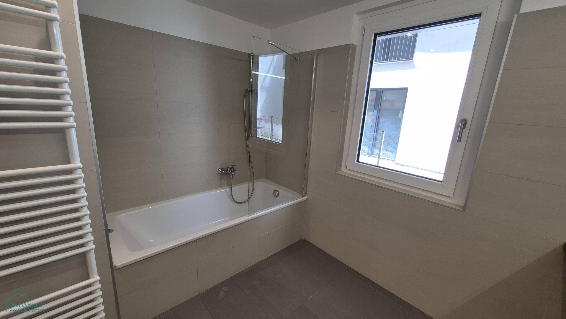 Modernes Badezimmer mit Badewanne, Duschwand und beheiztem Handtuchhalter, hell gefliest.