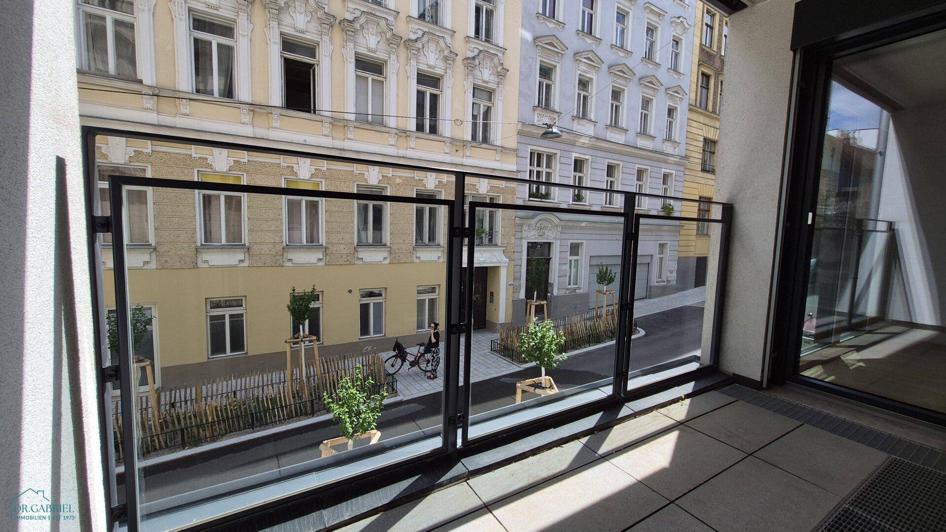 Heller Balkon mit Glasgeländer und Blick auf die gegenüberliegenden Gebäude.