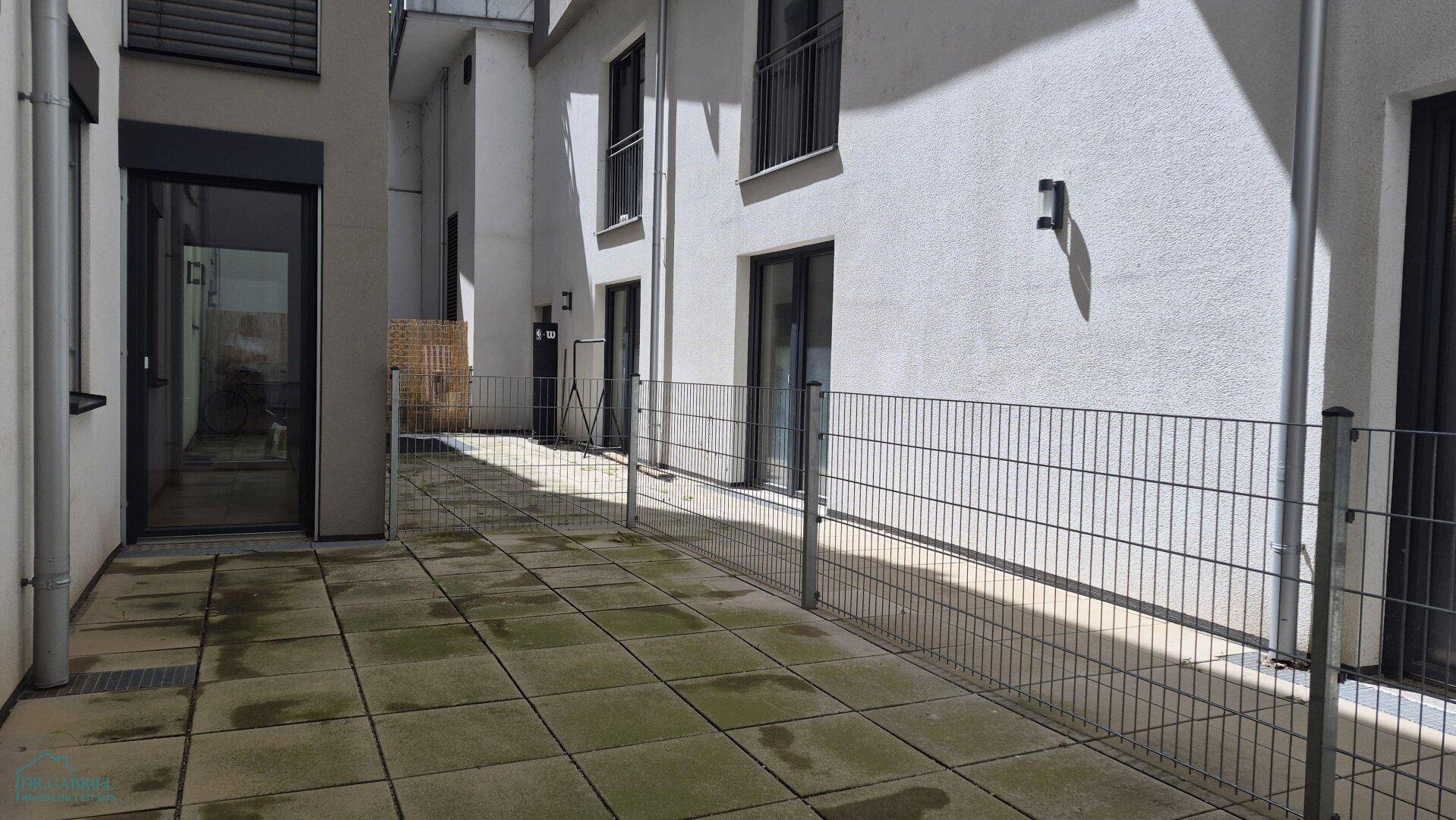 Weitläufige, gepflasterte Terrasse im Innenhof, umgeben von Gebäudefassaden.
