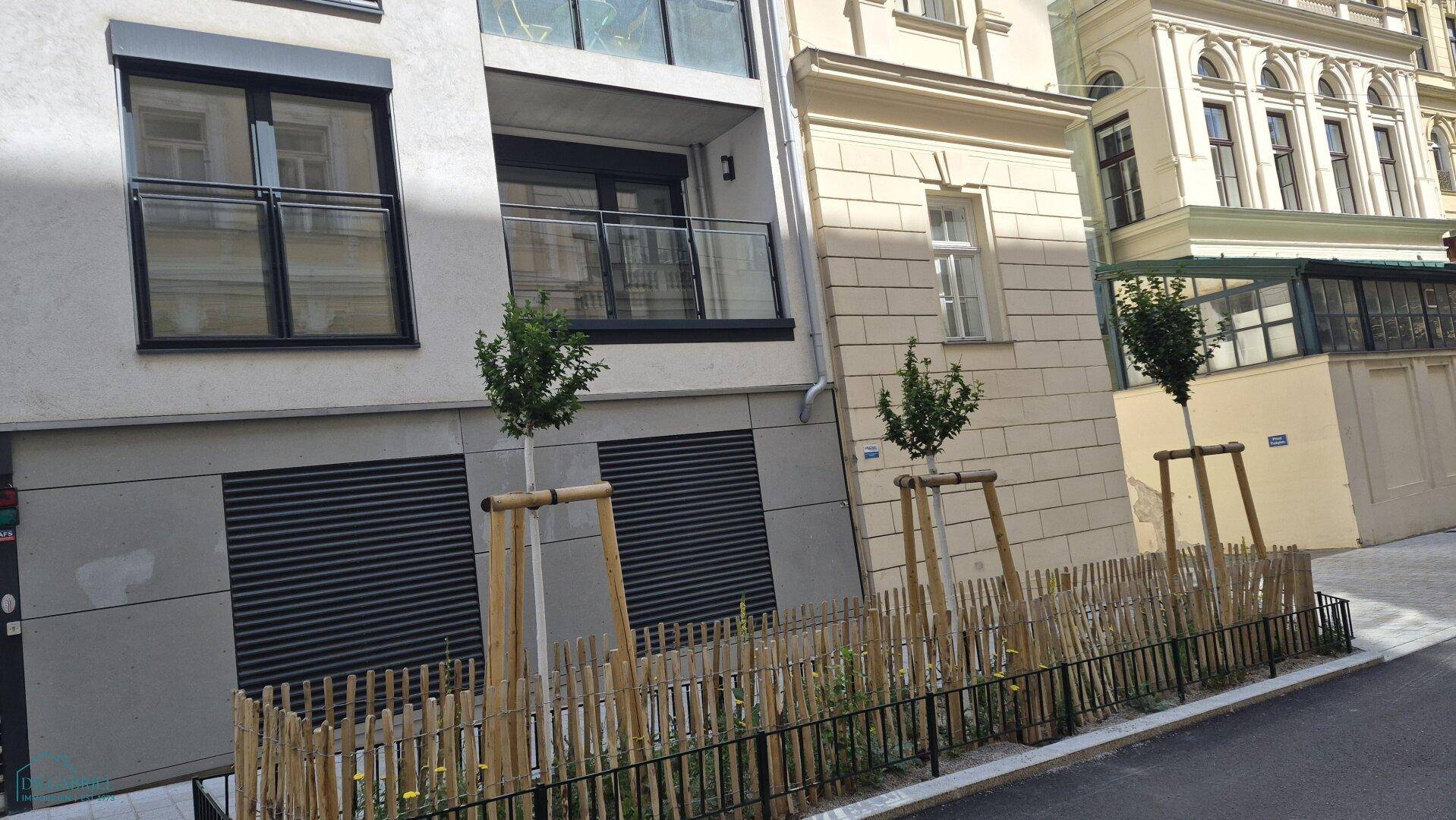 Moderne Gebäudefassade mit Balkonen und jungen Bäumen entlang der Straße.