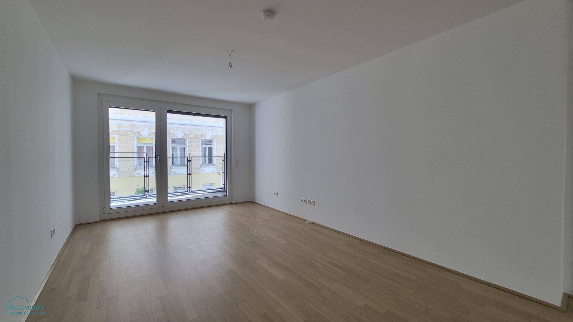 Geräumiges, leeres Wohnzimmer mit hellem Parkettboden und großen Fenstern.