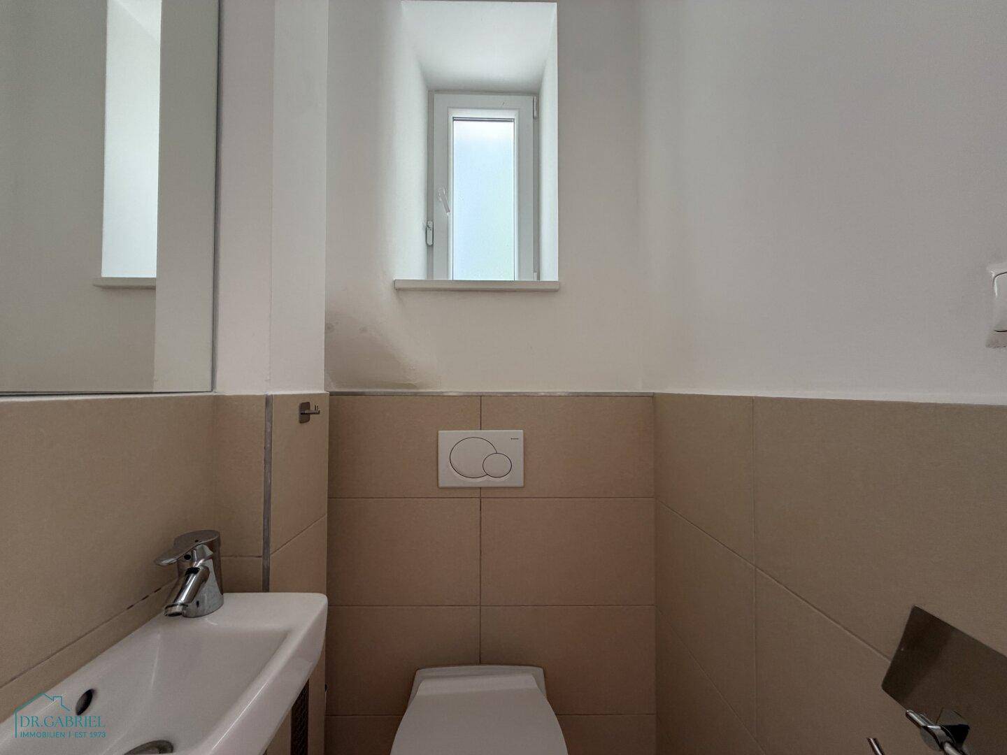 Kleines Gäste-WC mit Waschbecken, Toilette und einem schmalen Fenster.