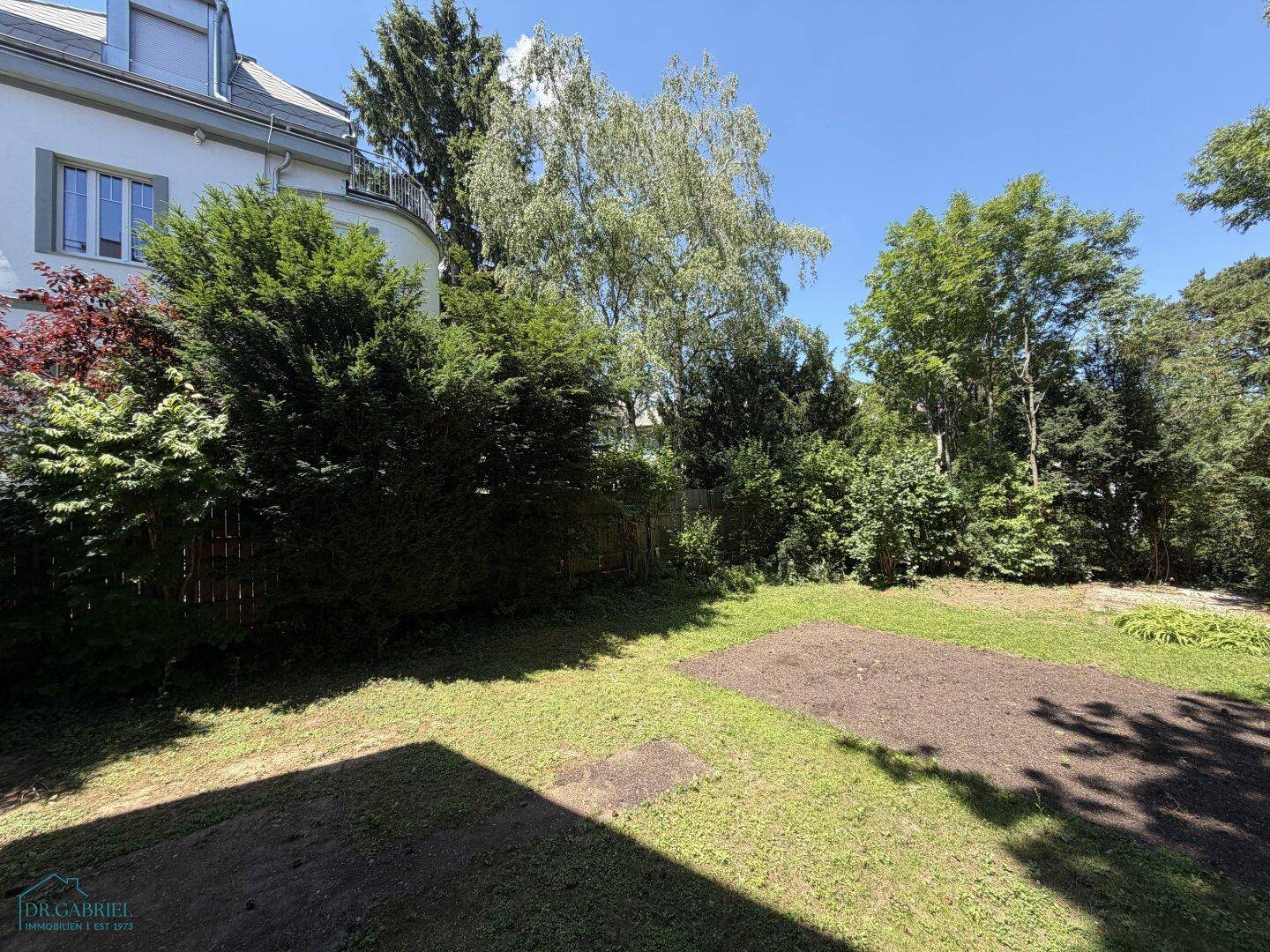 Großer Gartenbereich mit Rasen und vorbereitetem Beet, angrenzend an die Hausfassade.