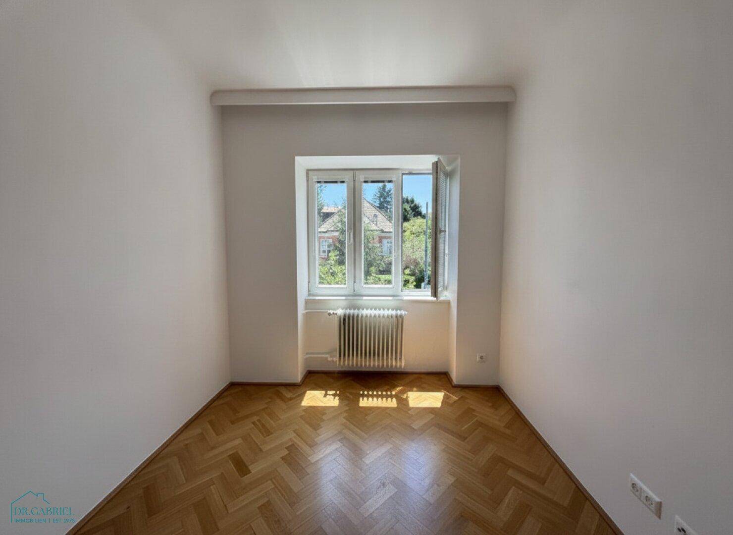 Gemütliches Schlafzimmer mit Fischgrätparkettboden und einem großen Fenster.