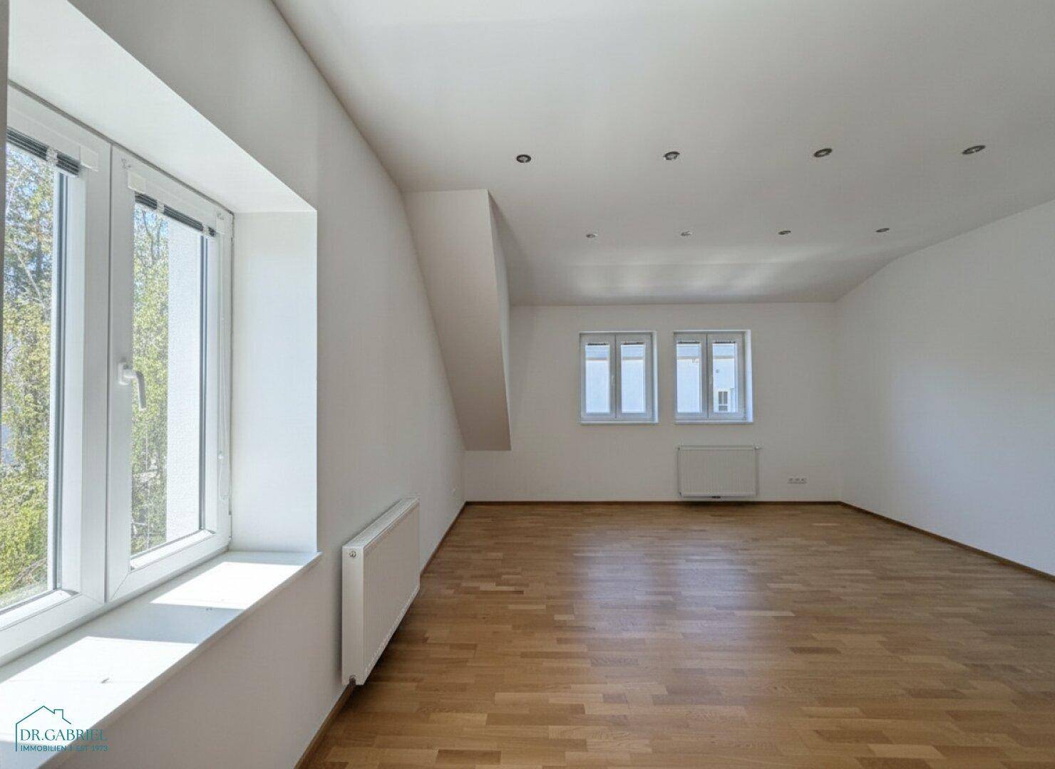 Geräumiger Dachgeschossraum mit Parkettboden, Einbaustrahlern und schrägen Wänden.
