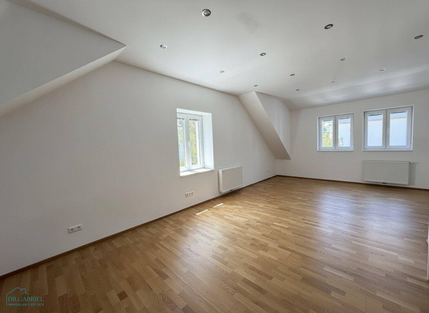 Heller Dachgeschossraum mit Parkettboden, Einbaustrahlern und schrägen Wänden.
