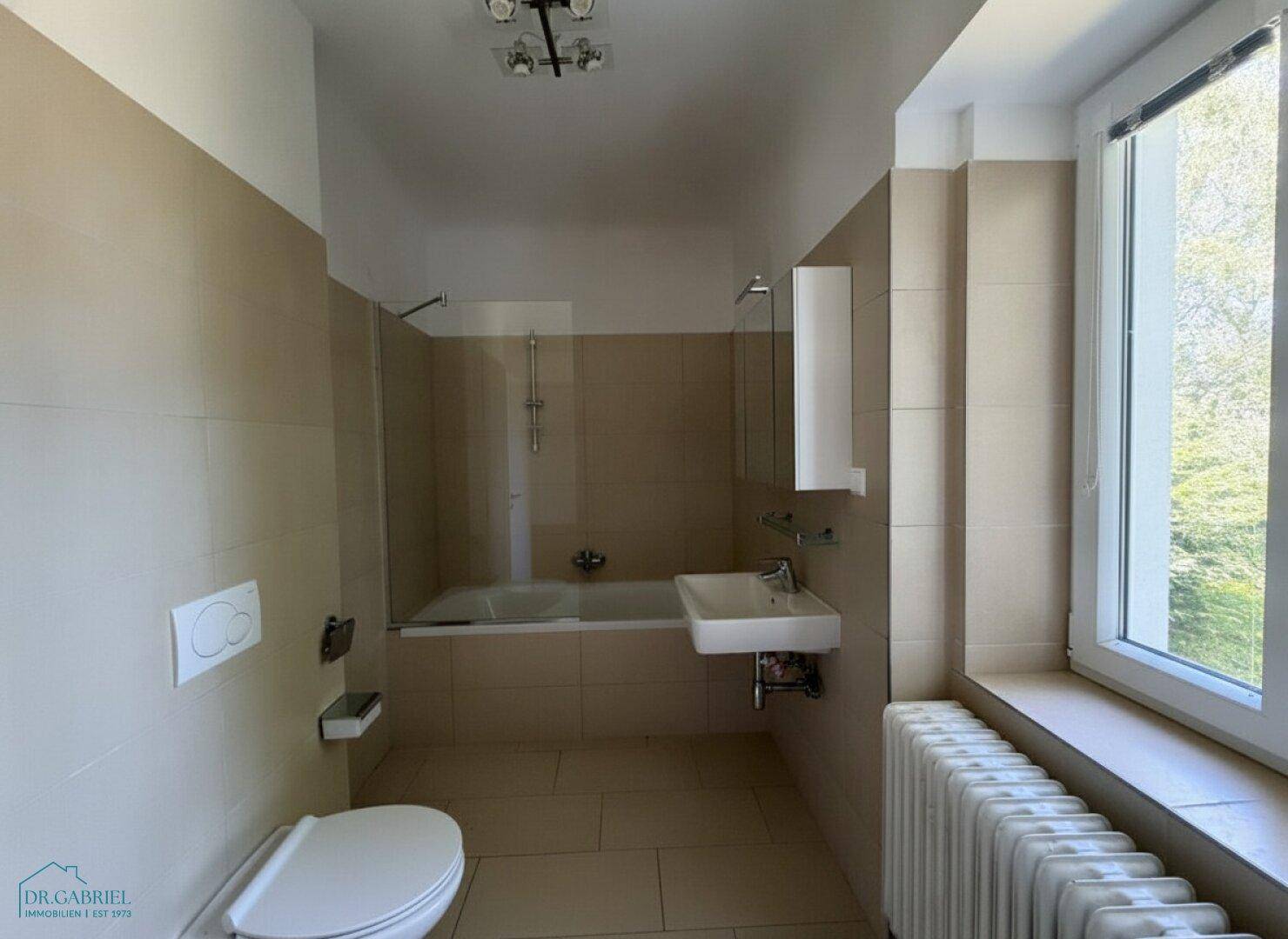 Gefliestes Badezimmer mit Badewanne, Waschbecken, Toilette und Fenster.