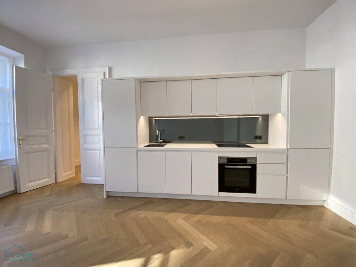 Moderne weiße Einbauküche mit integrierten Geräten und Fischgrätparkettboden.