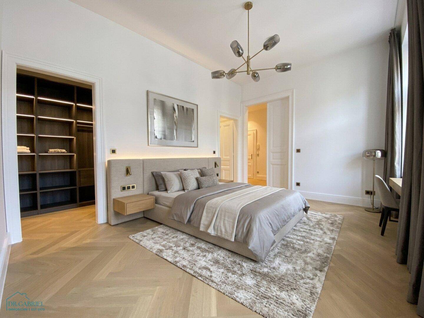 Elegantes Schlafzimmer mit Fischgrätparkett, hohen Decken und offenem Ankleidebereich.