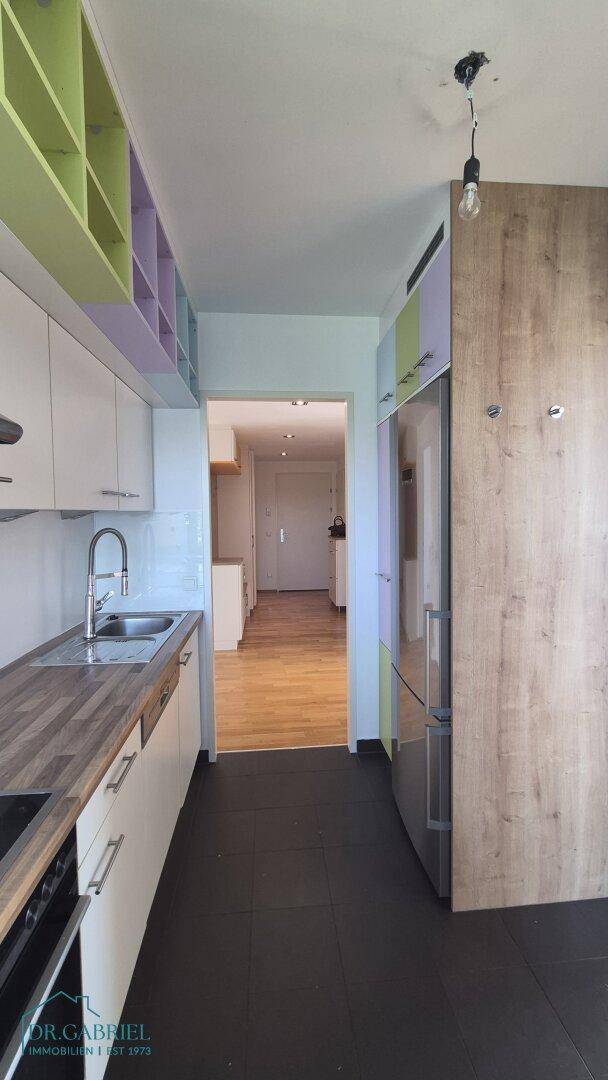 Schmale Küche mit weißen Schränken, Holzarbeitsplatte und integriertem Kühlschrank.