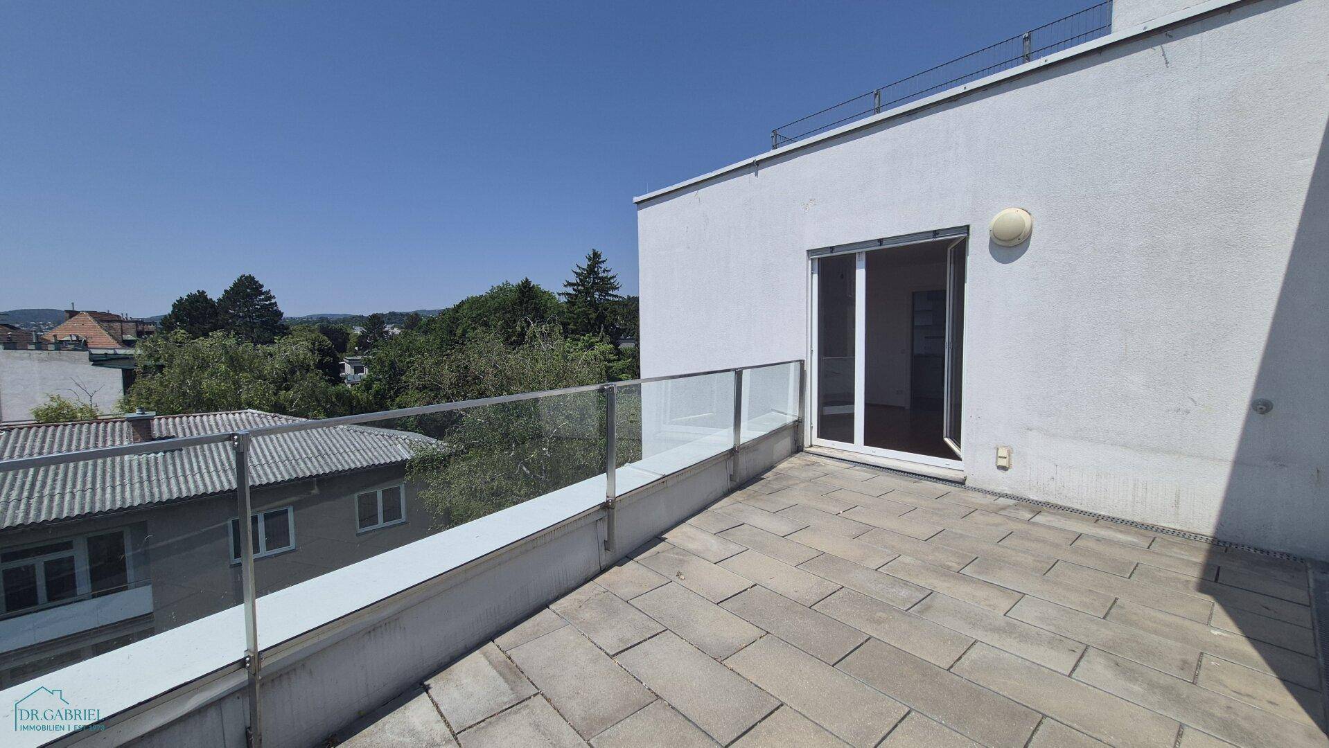 Helle Terrasse mit Steinplatten und Glasgeländer, direktem Zugang zum Innenbereich.