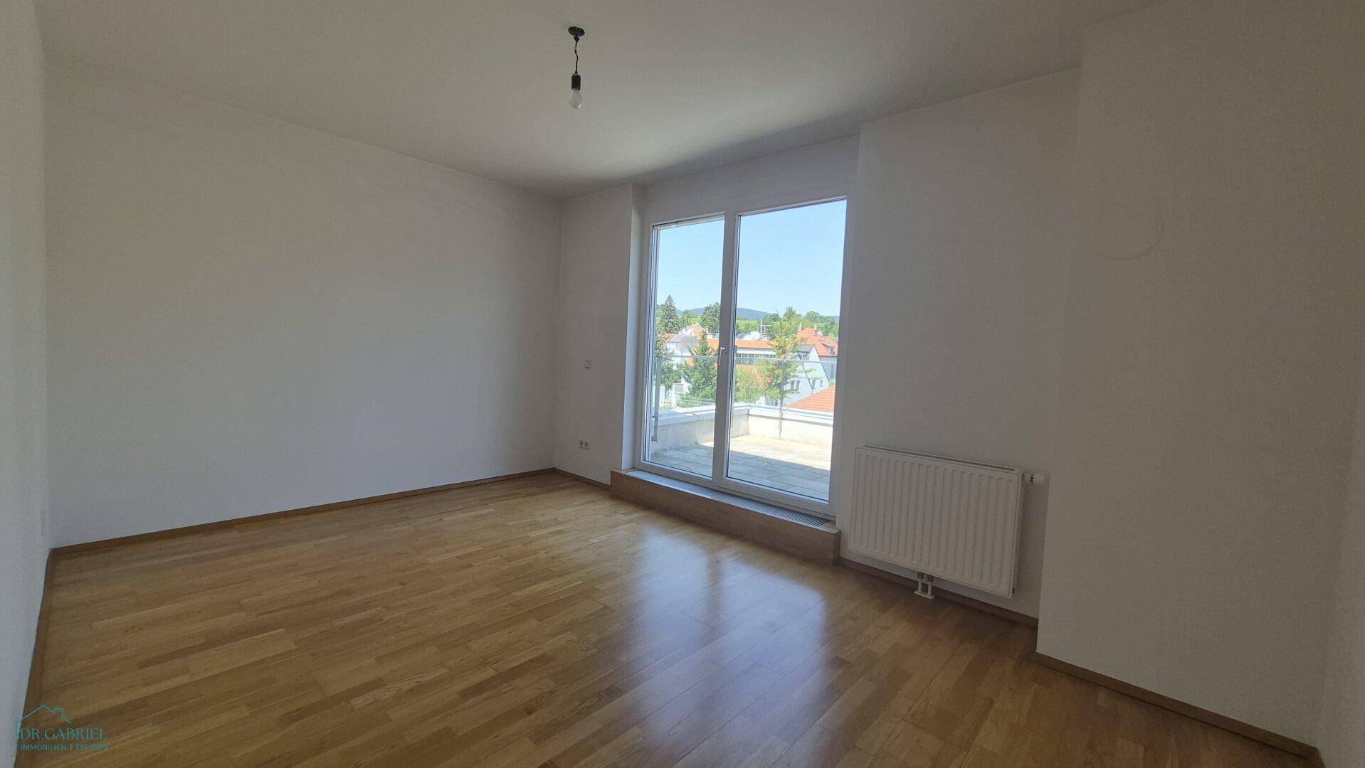 Leeres Schlafzimmer mit Holzboden, großen Fenstern und viel Tageslicht.
