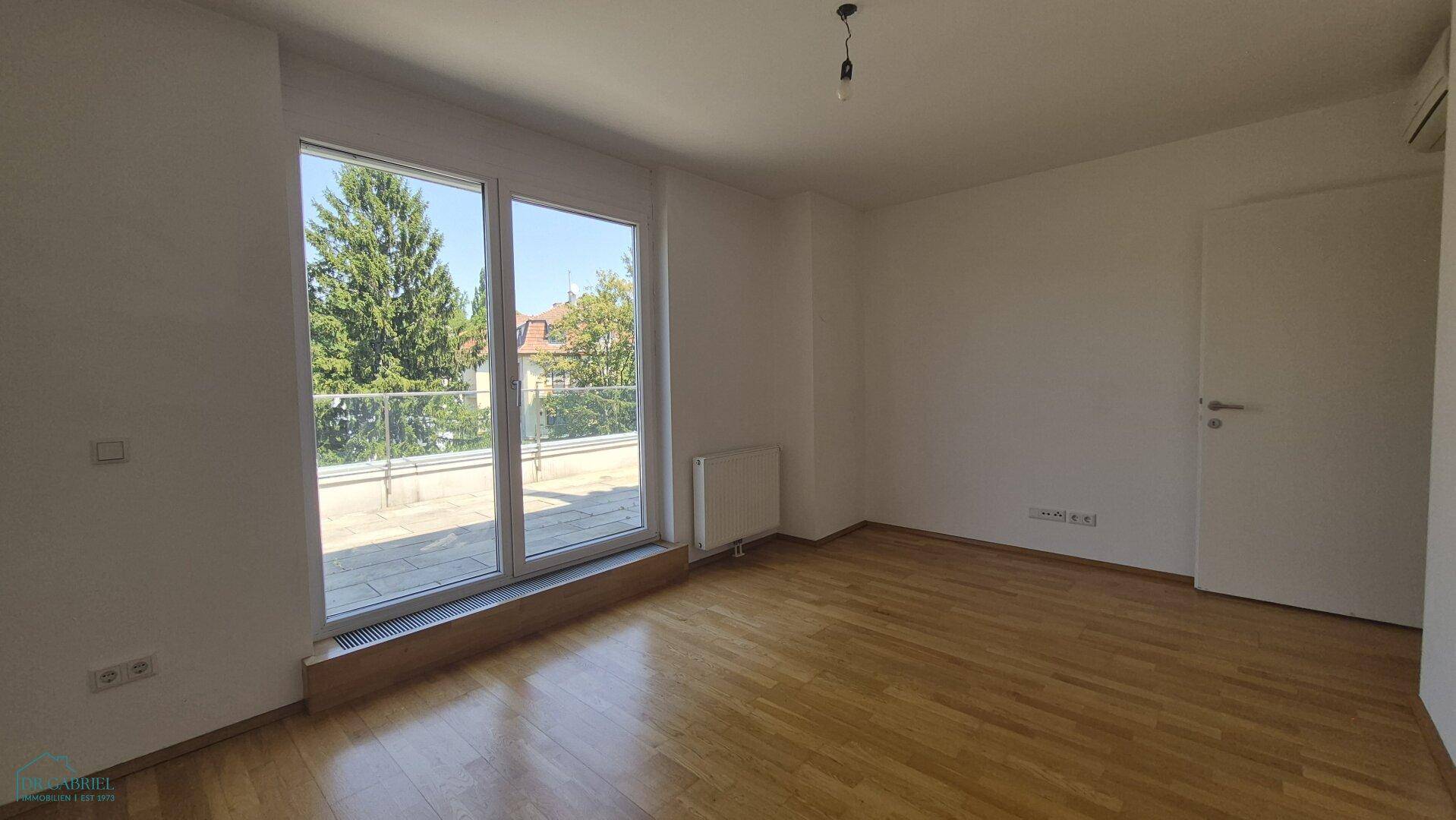 Geräumiges Schlafzimmer mit Holzboden, großen Fenstern und Zugang zur Terrasse.