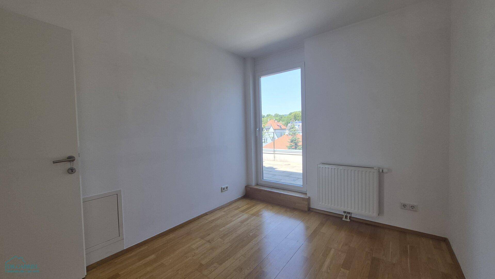 Leeres Zimmer mit Holzboden, Fenster und Heizkörper.