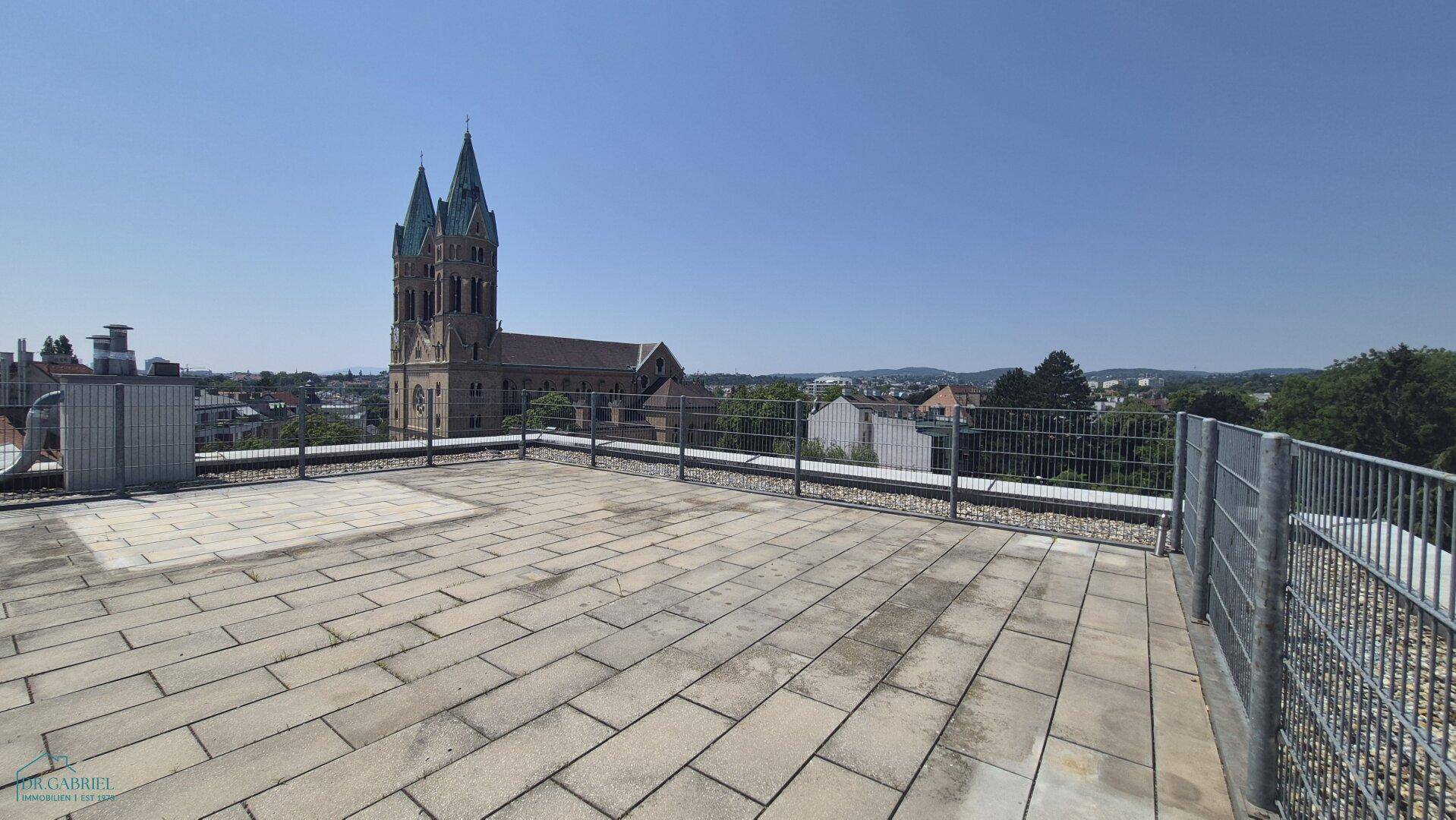 Geräumige Dachterrasse mit Steinplatten und weitem Blick über die Stadt und die Kirche.