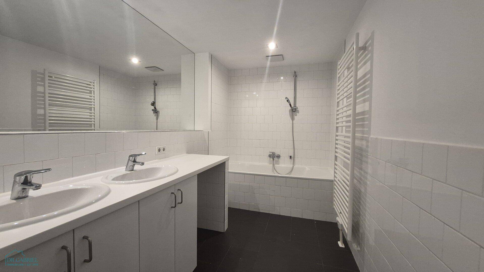 Modernes Badezimmer mit Doppelwaschbecken, Badewanne mit Dusche und beheiztem Handtuchhalter.