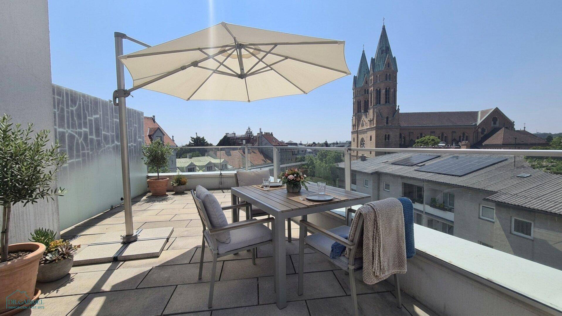 Gemütliche Terrasse mit Esstisch, Sonnenschirm und Blick auf die Stadt und die Kirche.