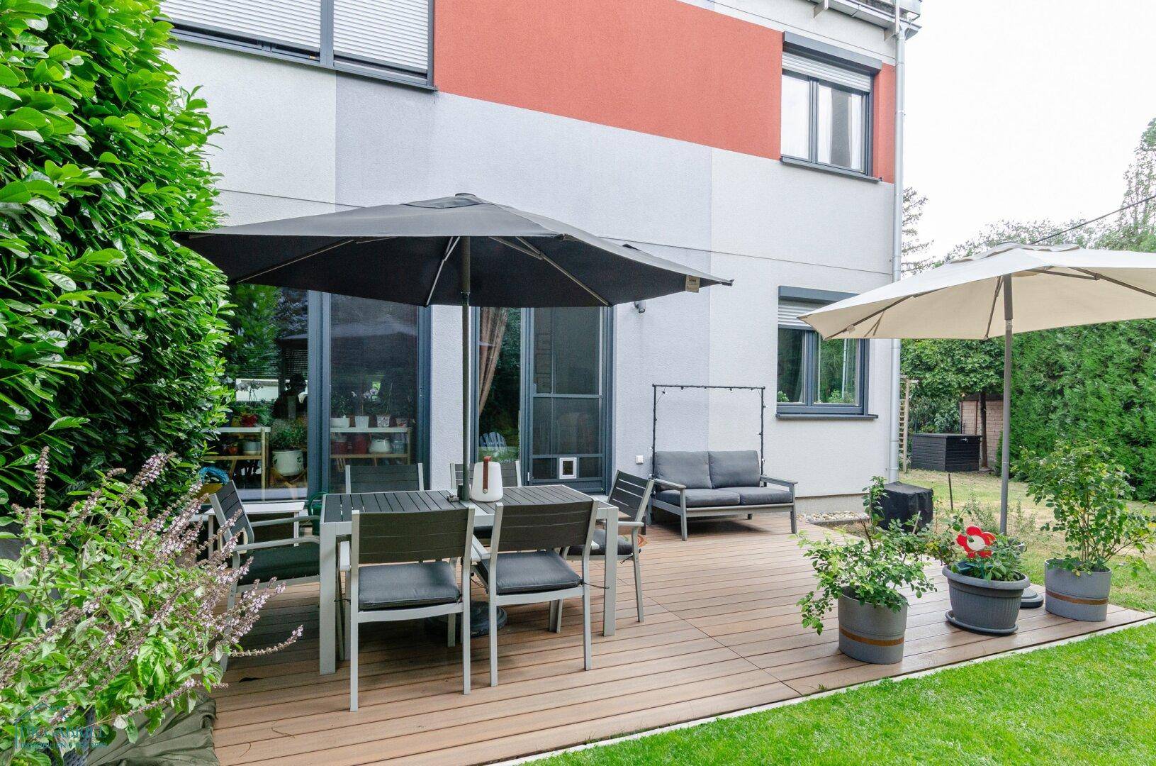 Gemütliche Terrasse mit Esstisch und Stühlen, umgeben von Grünflächen und Pflanzen.