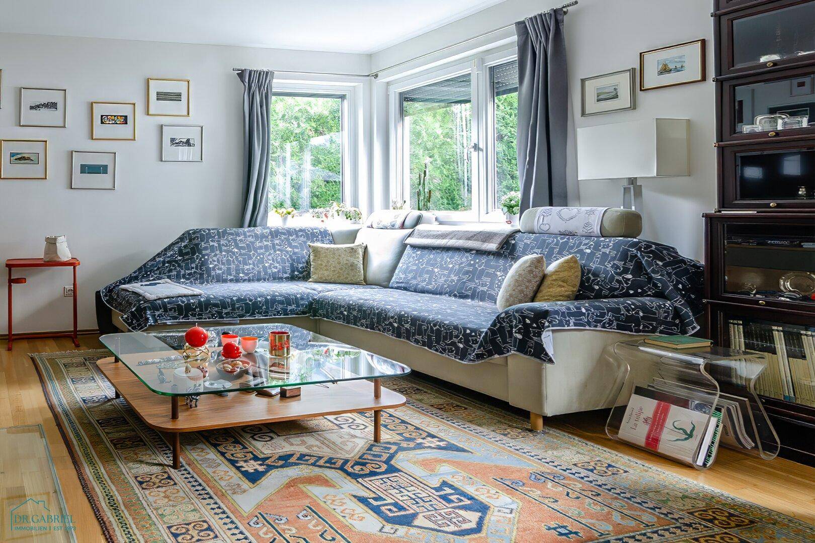 Helles Wohnzimmer mit großem Ecksofa, Couchtisch und Blick ins Grüne durch die Fenster.
