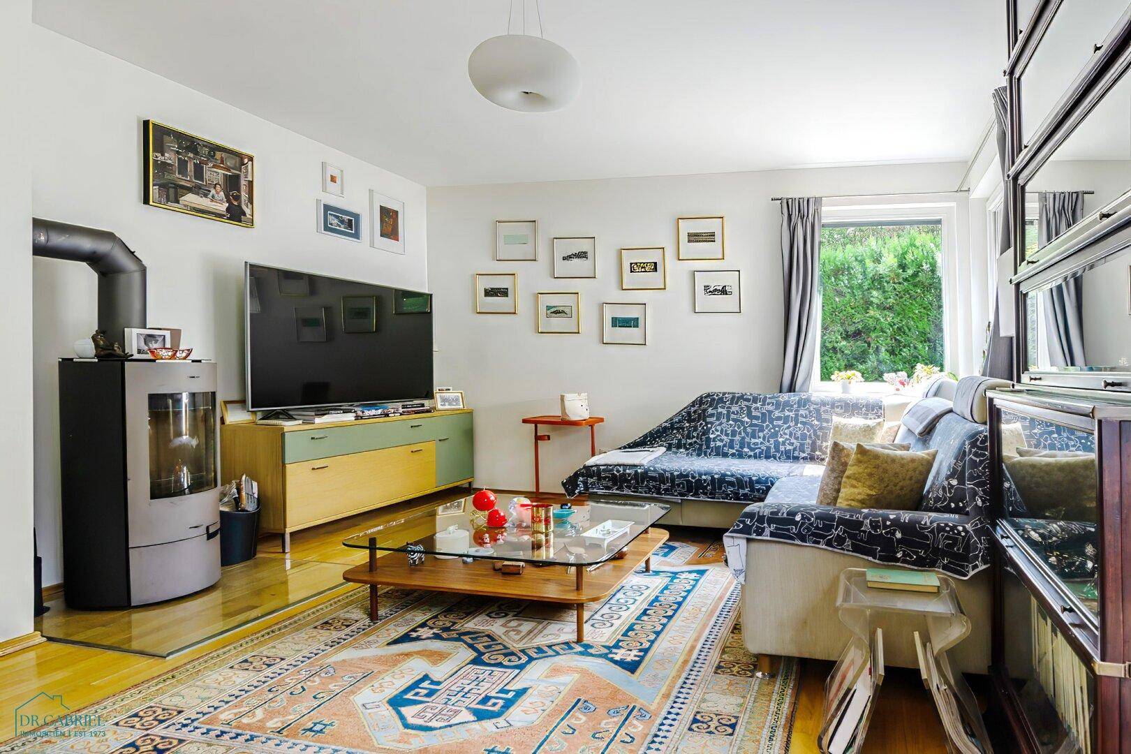 Gemütliches Wohnzimmer mit modernem Holzofen, Fernseher und bequemer Sitzecke.