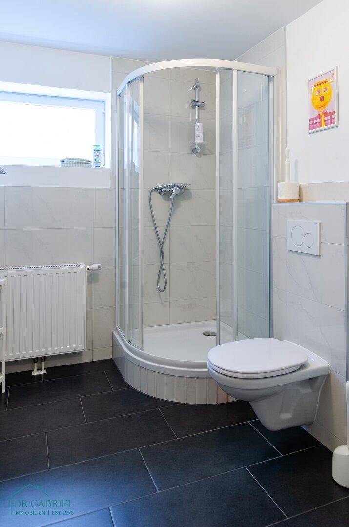 Badezimmer mit Eckdusche, wandhängendem WC und Fenster für natürliche Belüftung.