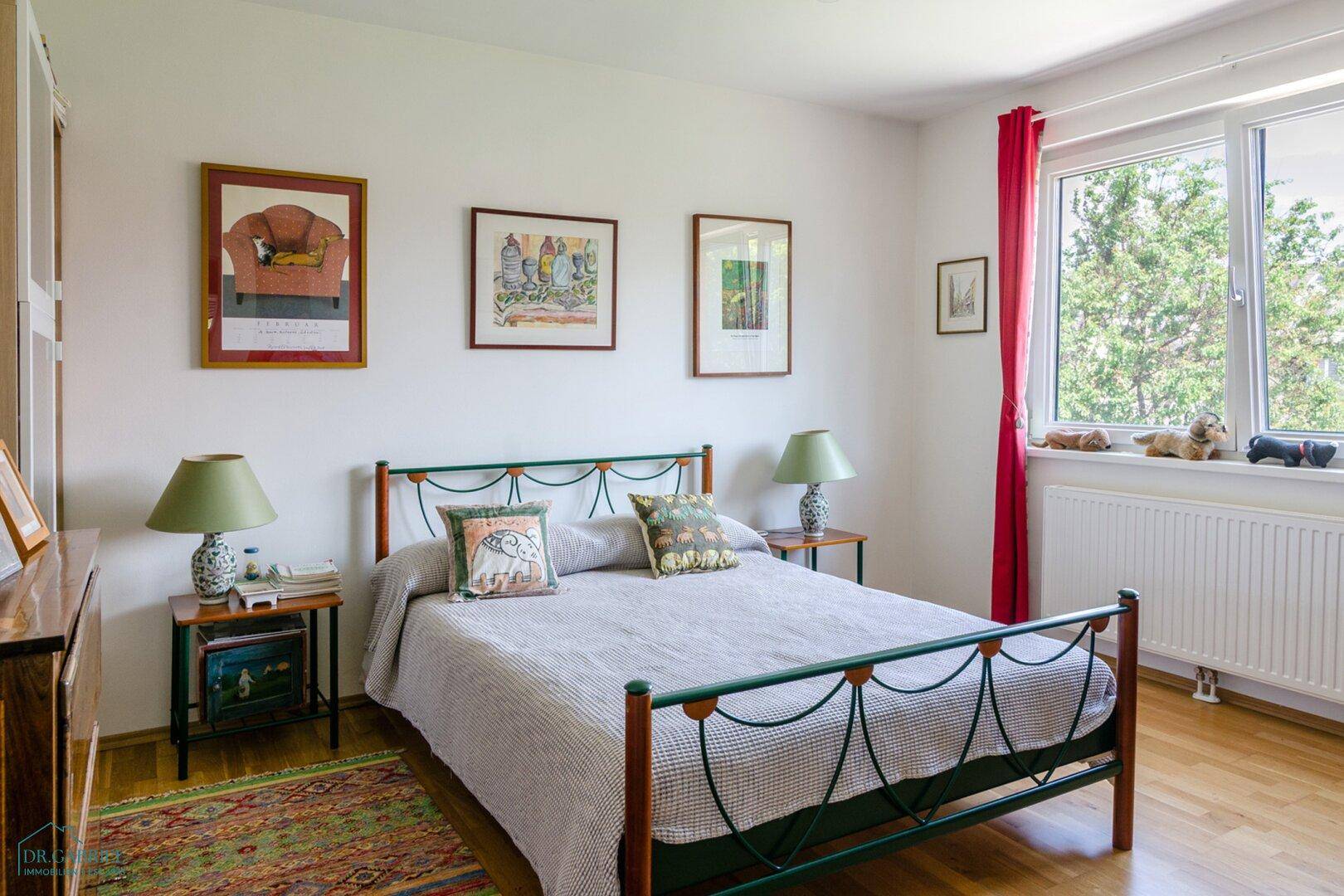 Gemütliches Schlafzimmer mit Metallbett, Nachttischen und einem Fenster mit Blick ins Grüne.