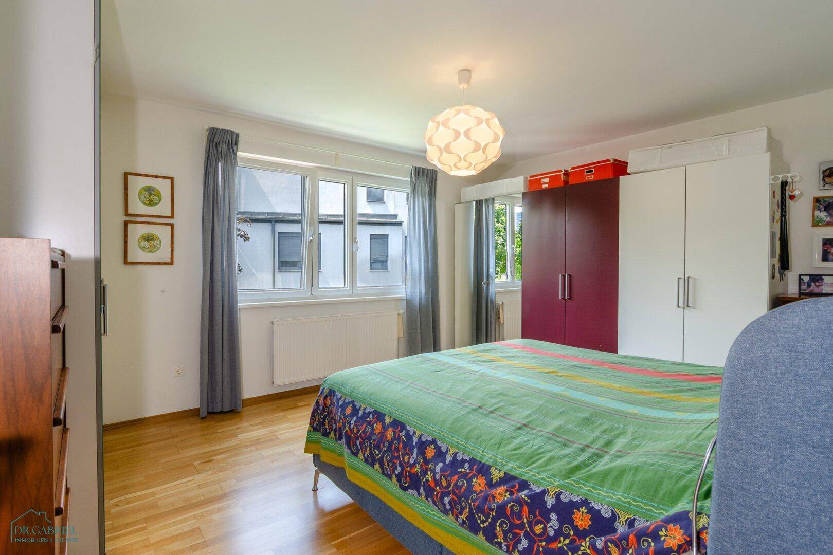 Helles Schlafzimmer mit großem Bett, Kleiderschränken und viel Tageslicht durch das Fenster.