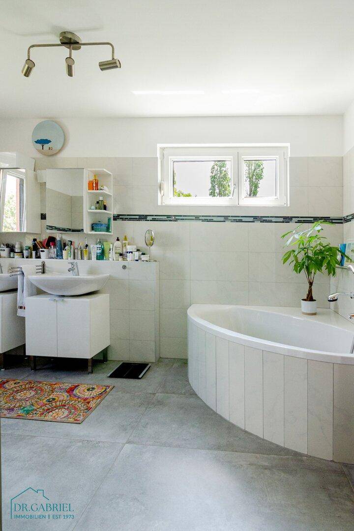 Geräumiges Badezimmer mit Badewanne, Doppelwaschbecken und einem Fenster für Tageslicht.