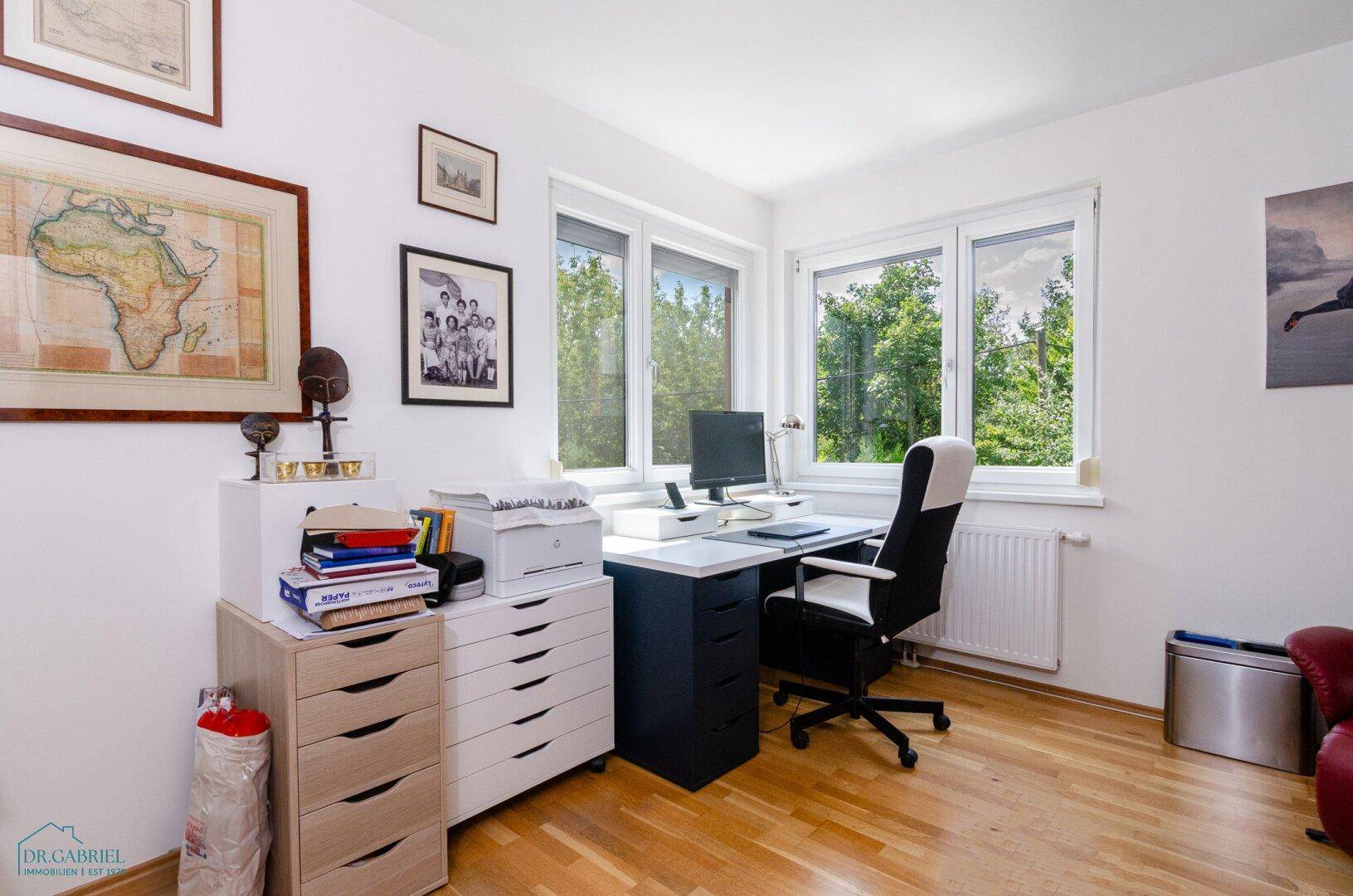 Funktionales Heimbüro mit Schreibtisch, Bürostuhl und Fenstern mit Blick ins Grüne.