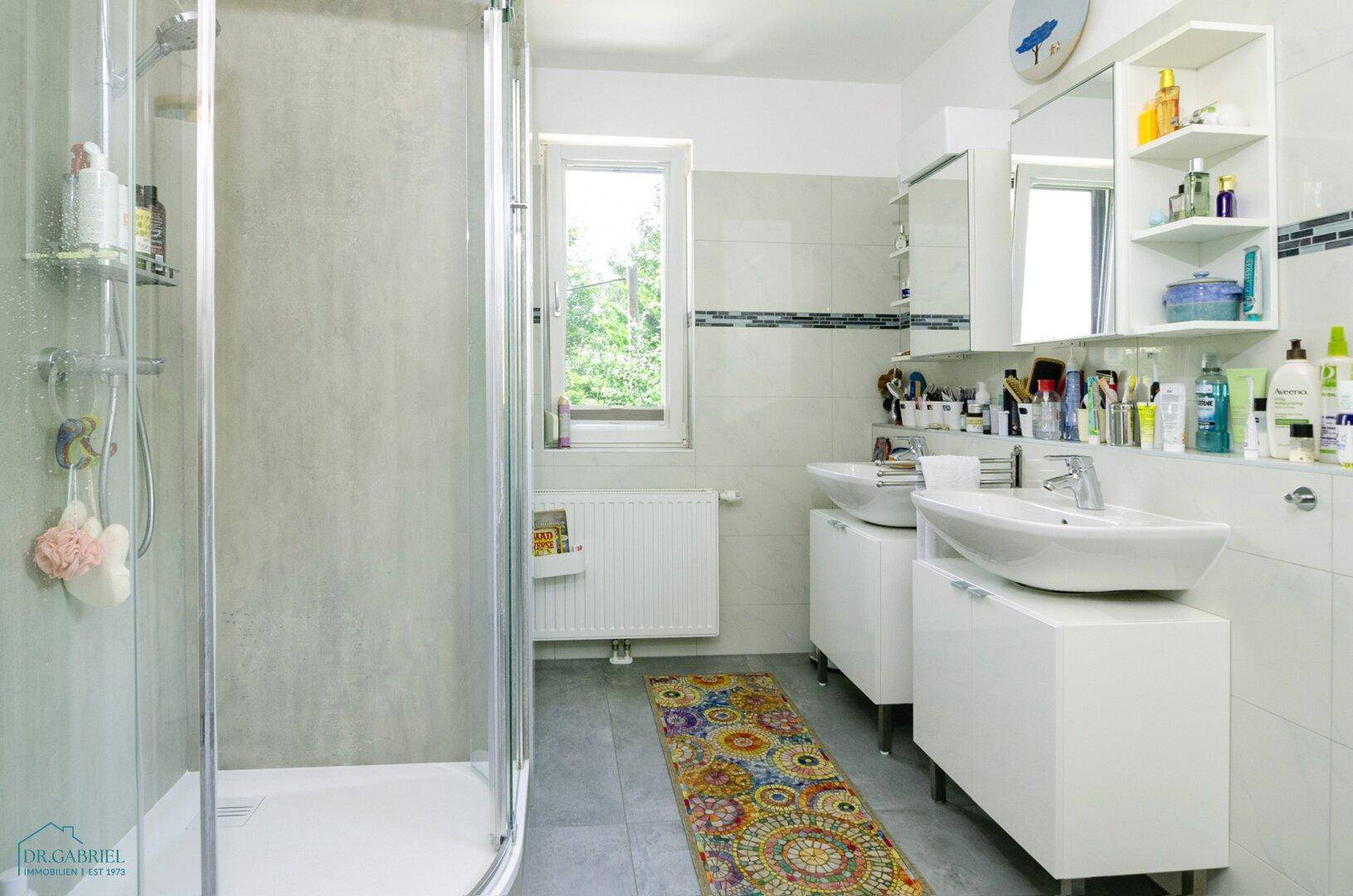 Helles Badezimmer mit Duschkabine, Doppelwaschbecken und Fenster für gute Belüftung.