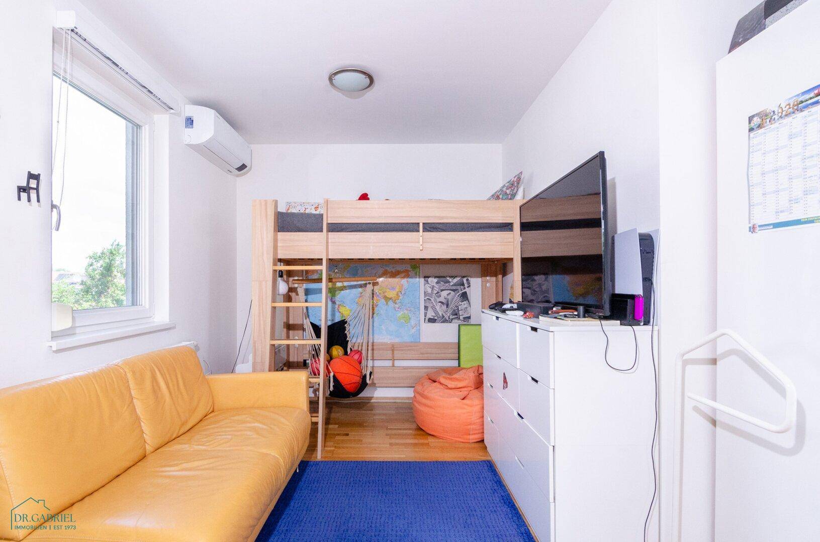Kinderzimmer mit Hochbett, Sofa und Klimaanlage für angenehmes Raumklima.