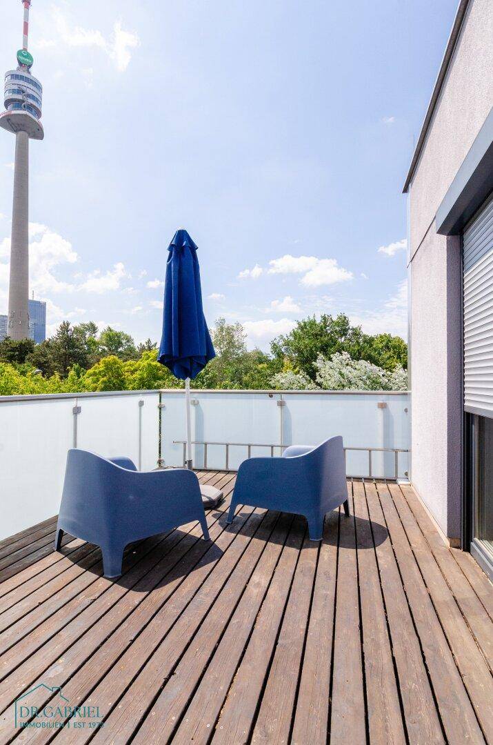 Dachterrasse mit Sitzgelegenheiten und weitem Blick auf die Umgebung und einen Turm.