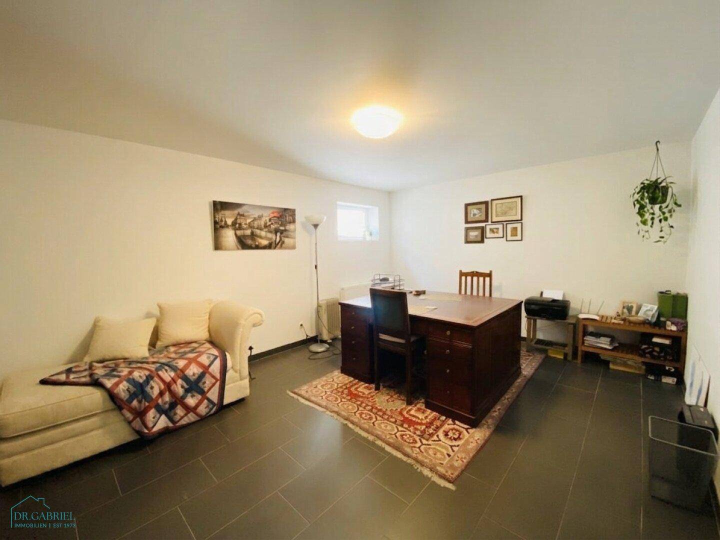 Geräumiger Kellerraum, nutzbar als Büro oder Gästezimmer, mit Schreibtisch und Sofa.