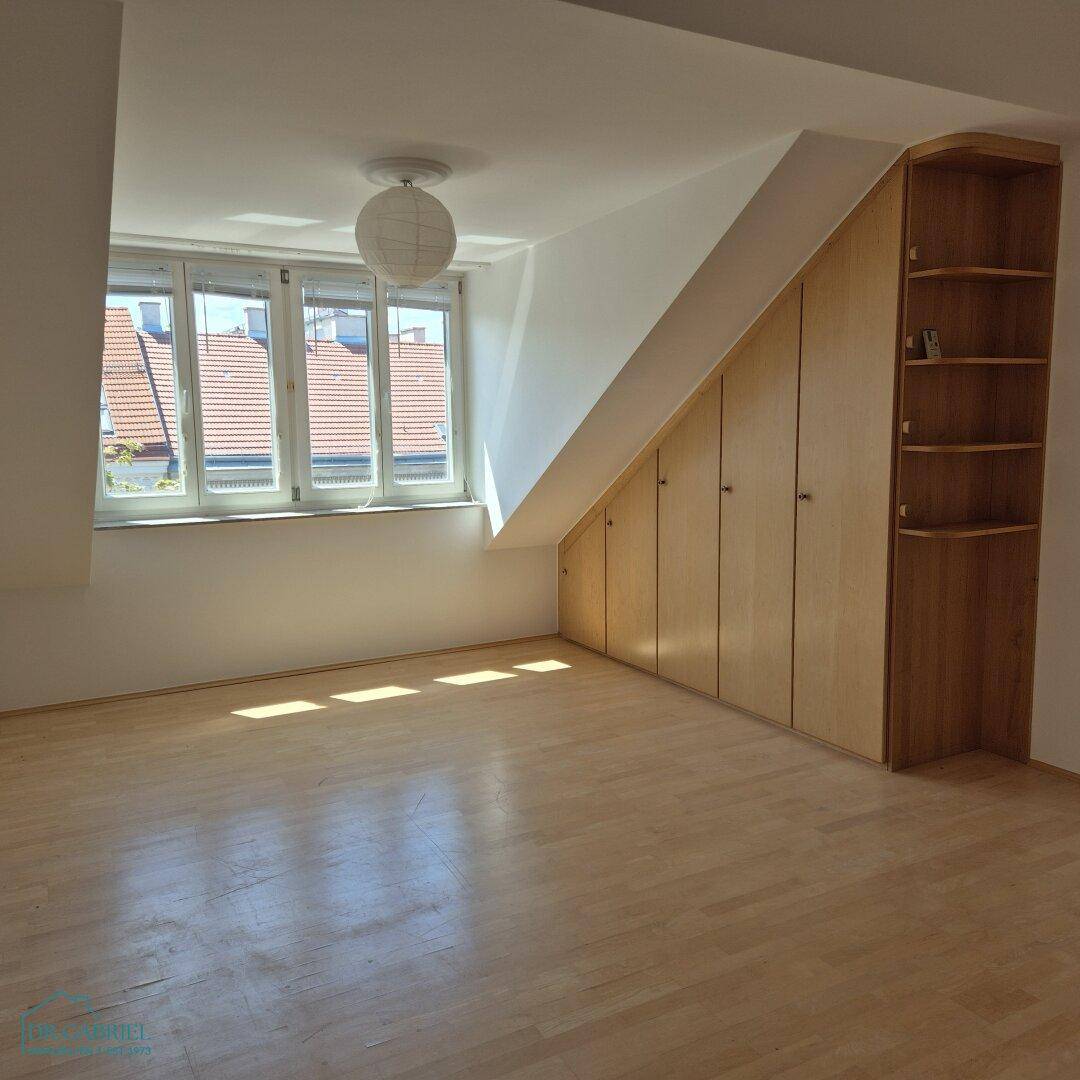 Dachgeschosszimmer mit schrägen Wänden, Einbauschränken und hellem Holzfußboden, der eine gemütliche Atmosphäre schafft.