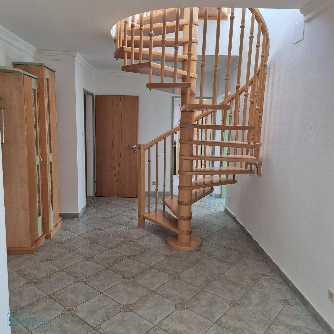 Heller Flur mit einer eleganten Holzwendeltreppe und Fliesenboden, der die verschiedenen Ebenen verbindet.