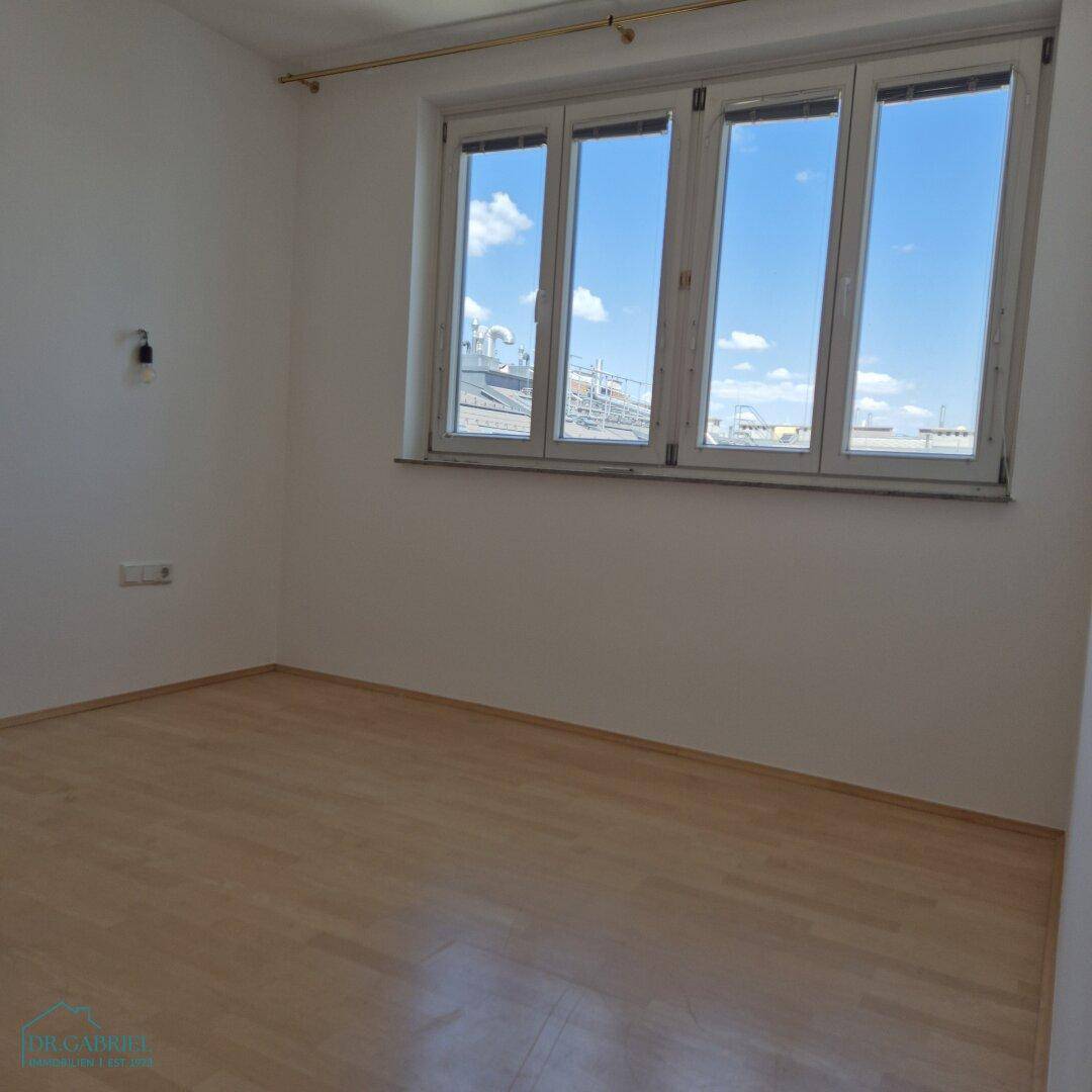 Heller Raum mit Holzfußboden und großen Fenstern, die einen weiten Blick über die Dächer ermöglichen.