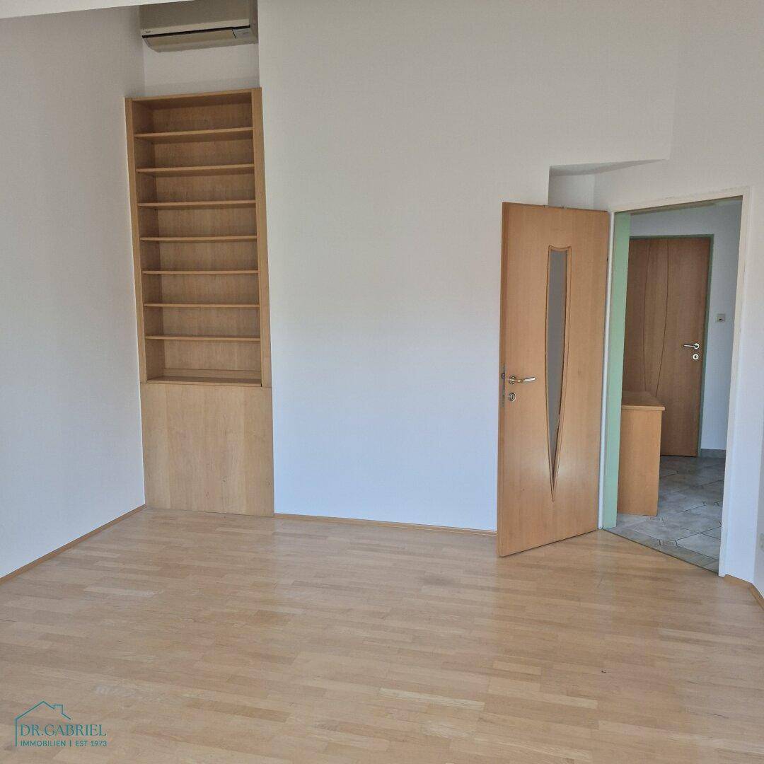 Heller Raum mit Holzfußboden und integriertem Regal, der vielseitig genutzt werden kann.