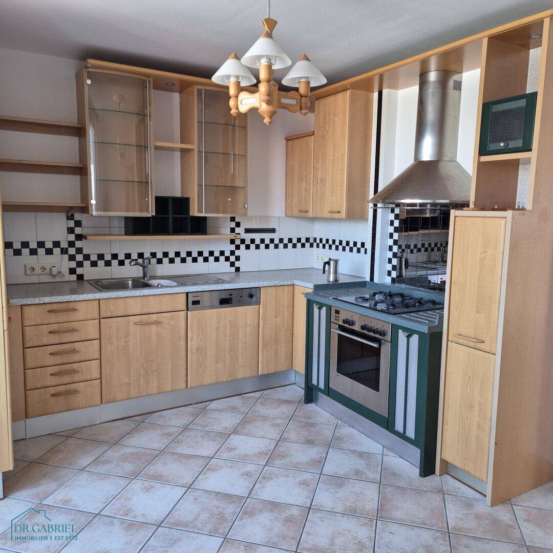Funktionale Küche mit hellen Holzschränken, kariertem Fliesenspiegel und integrierten Geräten.