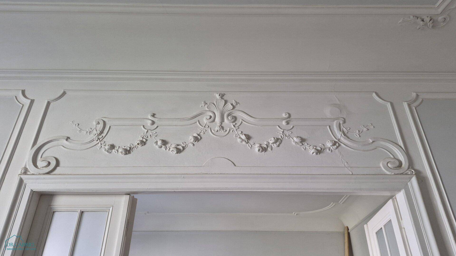 Detailaufnahme einer kunstvollen Stuckverzierung über einem Türrahmen, die den klassischen Stil des Raumes unterstreicht.