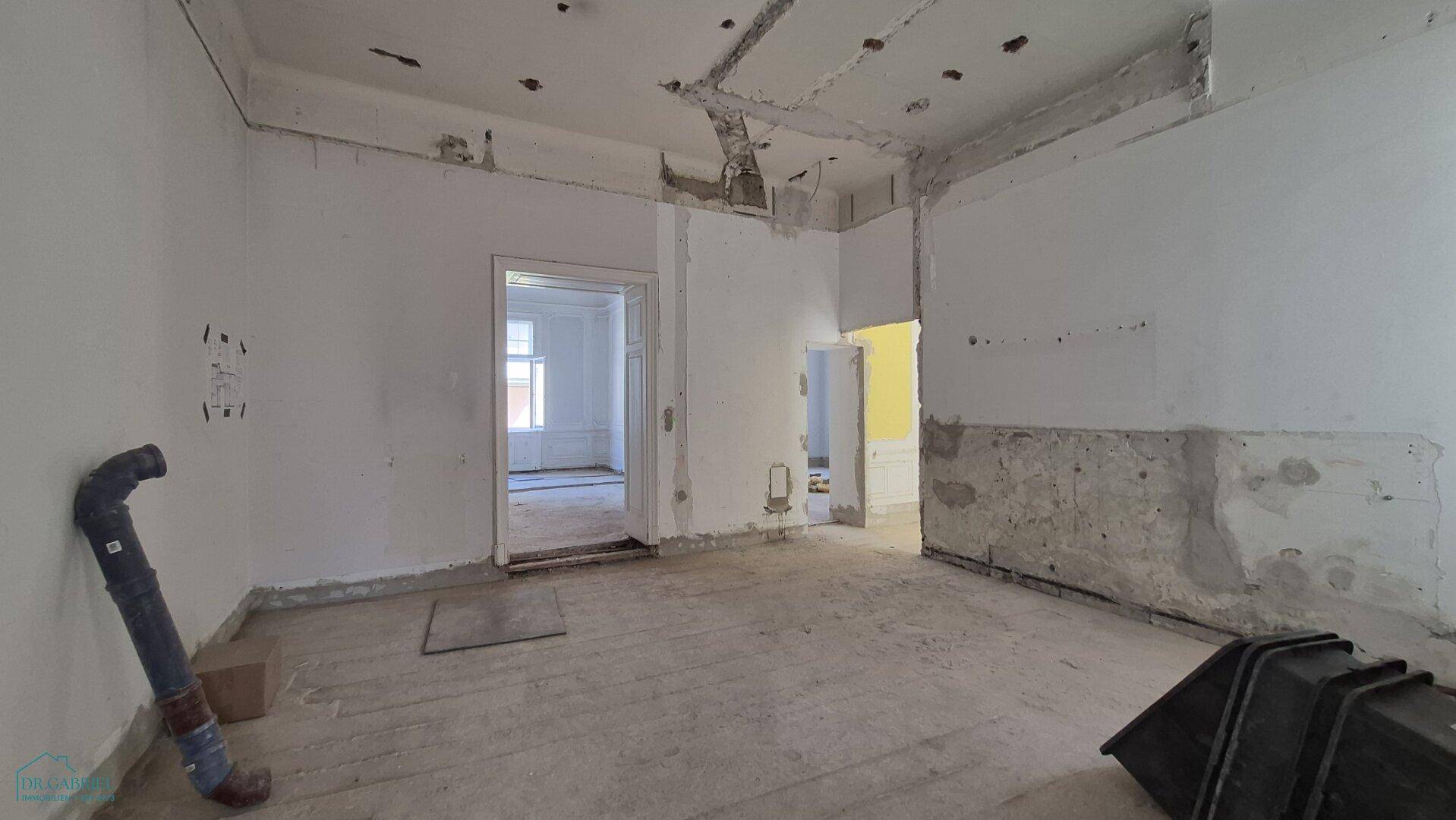 Großer Raum in Renovierung mit Betonboden und freigelegten Wänden, bereit für den Ausbau.