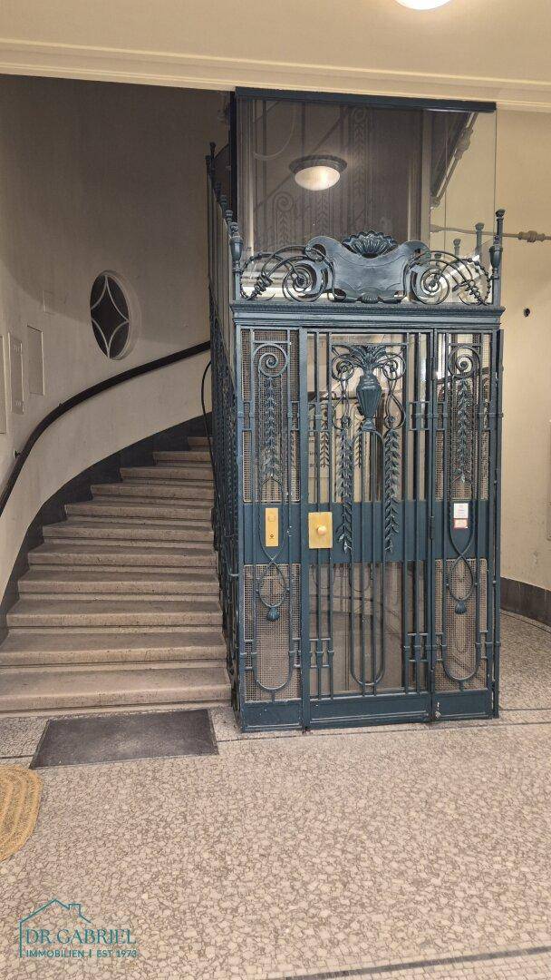 Detailansicht des historischen Aufzugs und der geschwungenen Treppe im Eingangsbereich.