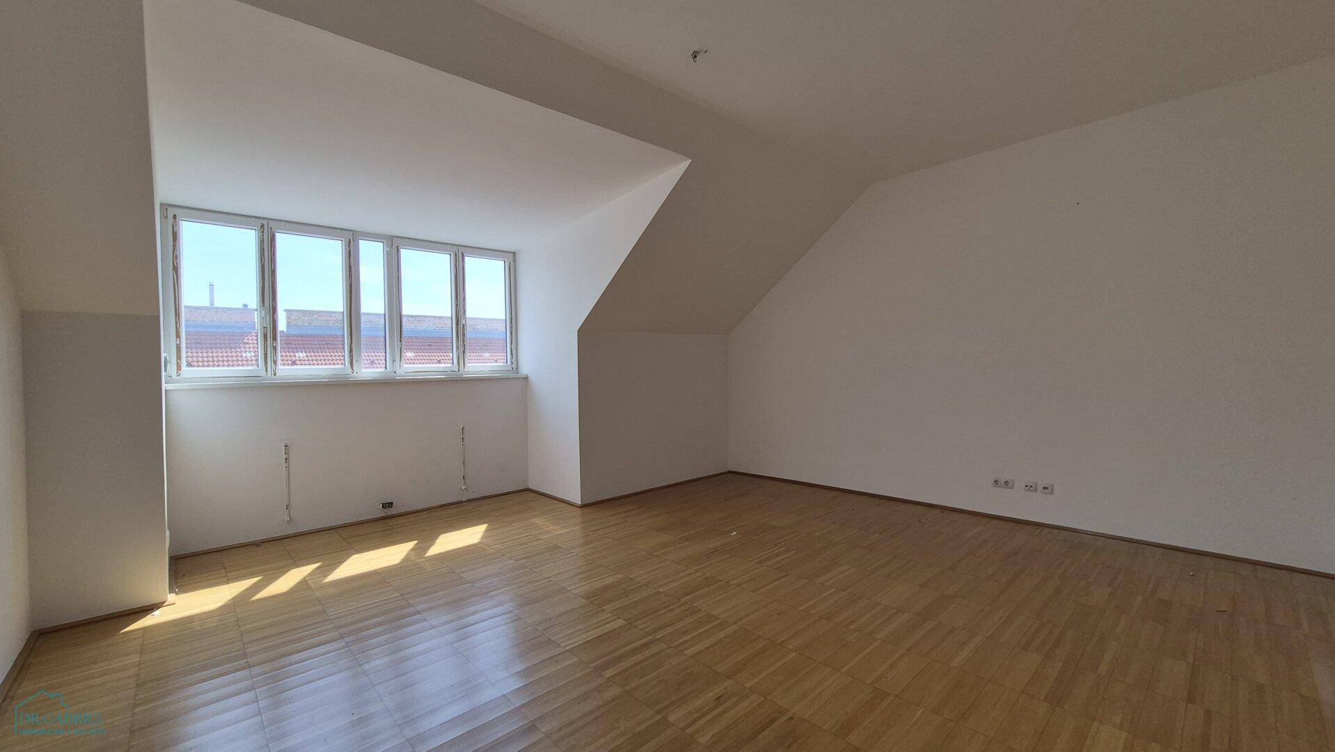 Helles, leeres Schlafzimmer mit Parkettboden, Dachschrägen und breiter Fensterfront.