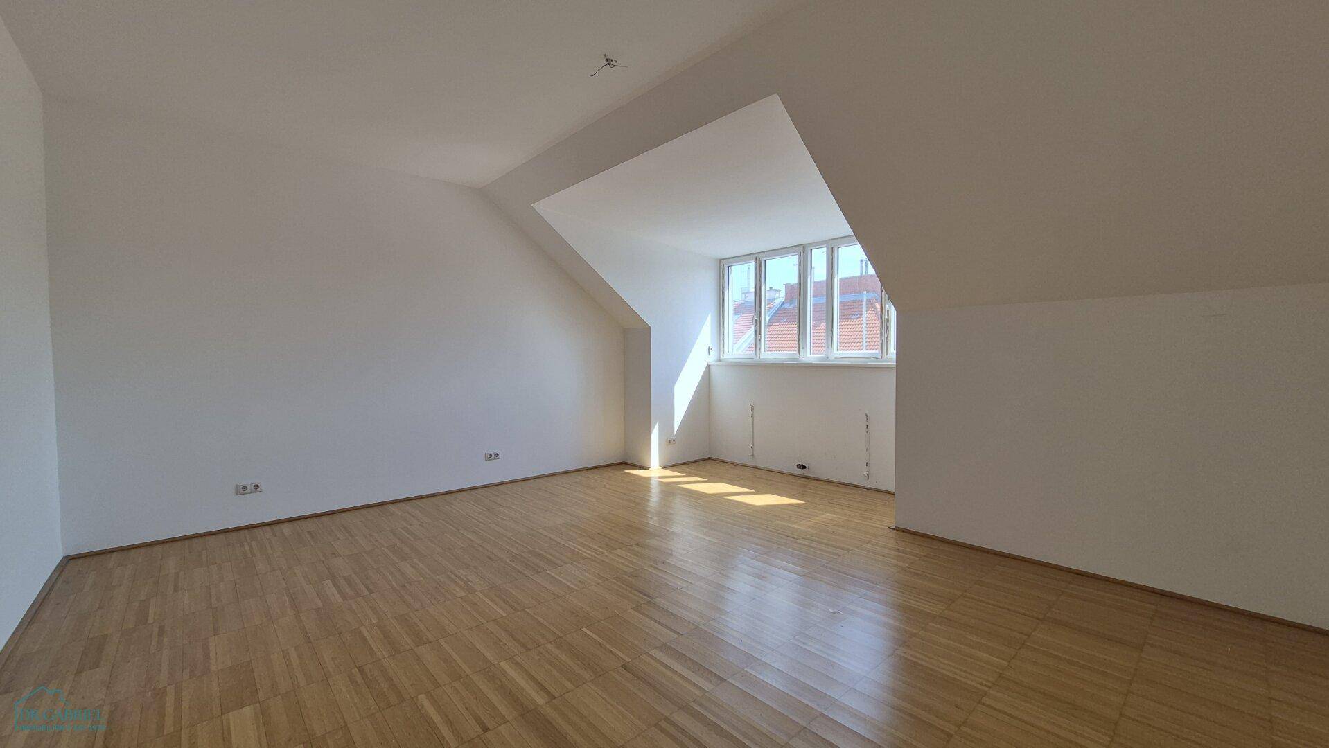Geräumiges, leeres Schlafzimmer mit Parkettboden, Dachschrägen und viel natürlichem Lichteinfall.